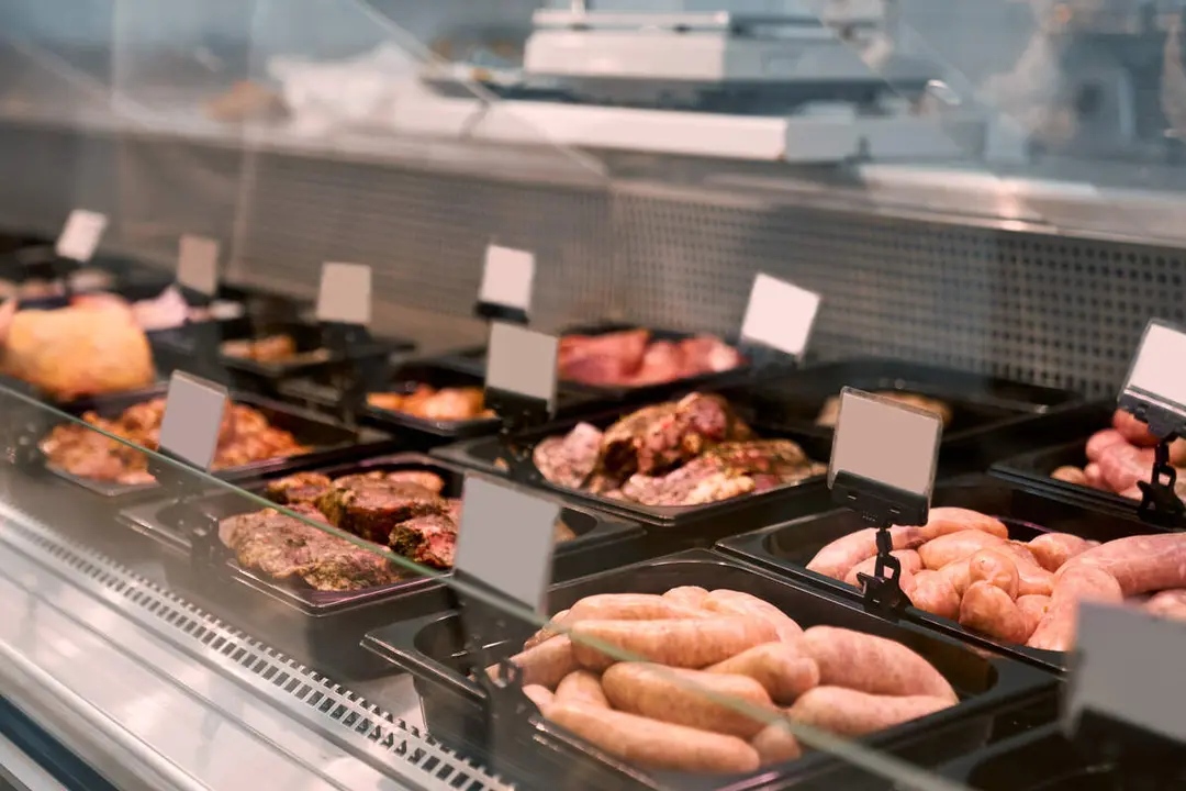 Close up of raw meat pieces and meat products in refrigerator with price tags ready for sale in meat department of store. Glass counter with plates of sliced fresh steaks. Concept of food.