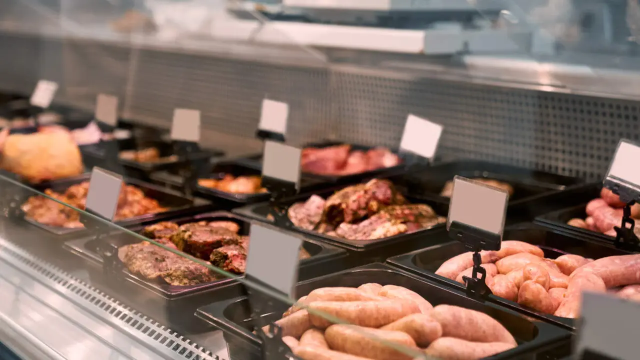 Close up of raw meat pieces and meat products in refrigerator with price tags ready for sale in meat department of store. Glass counter with plates of sliced fresh steaks. Concept of food.